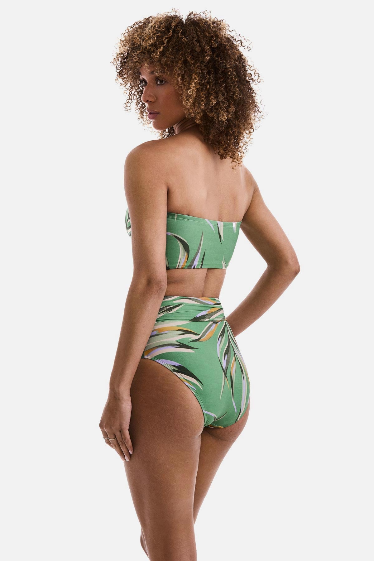Woman turned left wearing a multicolored leaf print bandeau midkini swim top with matching swim bottoms