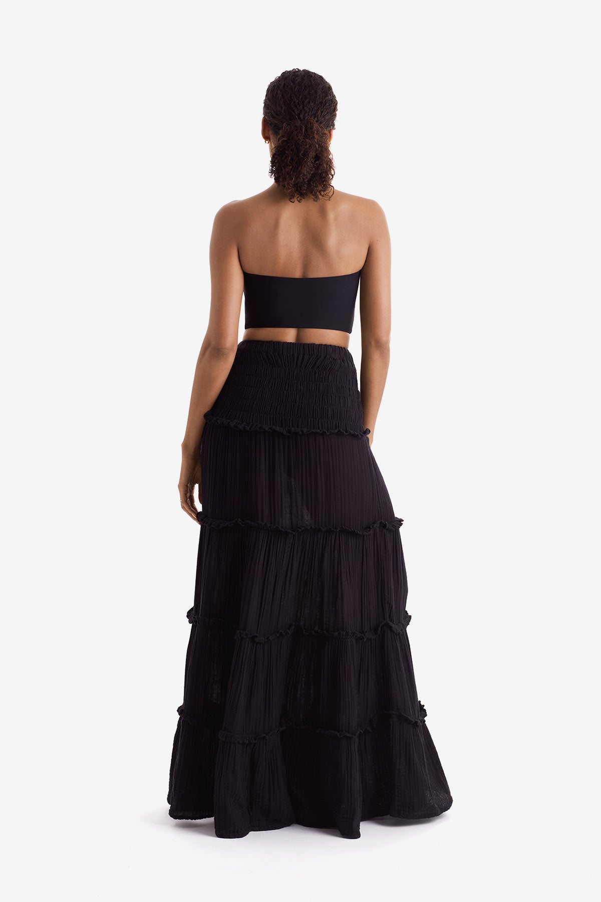 Woman turned away wearing a black bandeau top and black floor length skirt