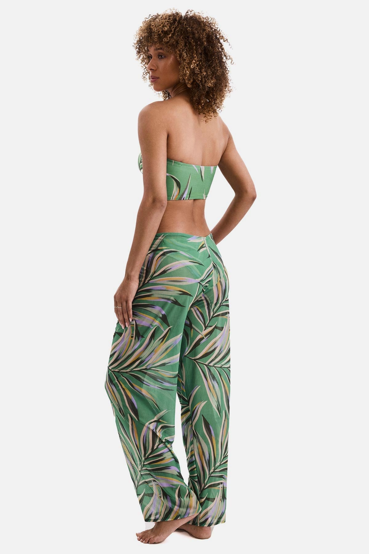 Woman turned left wearing a multicolored leaf printed swim cover up pants with a matching midkini top